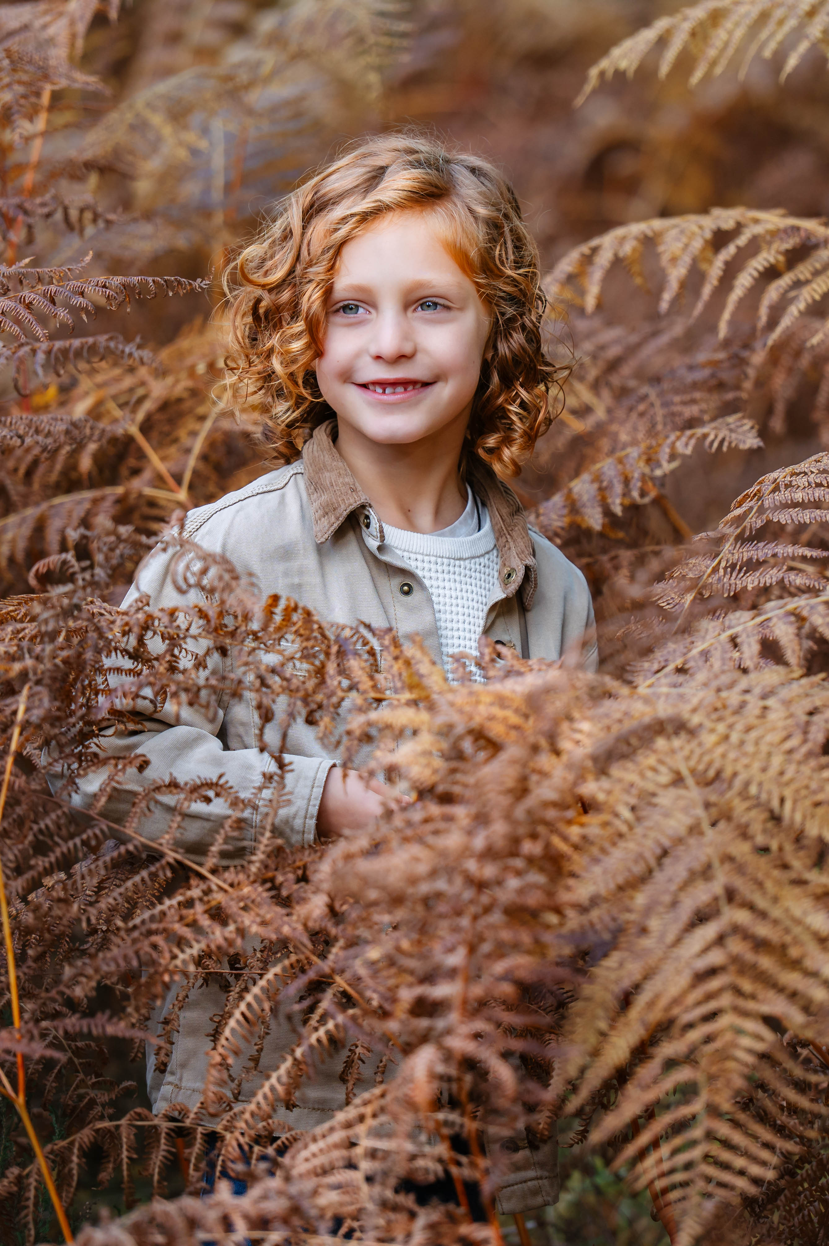 Child smiling among autumn ferns during an outdoor portrait session